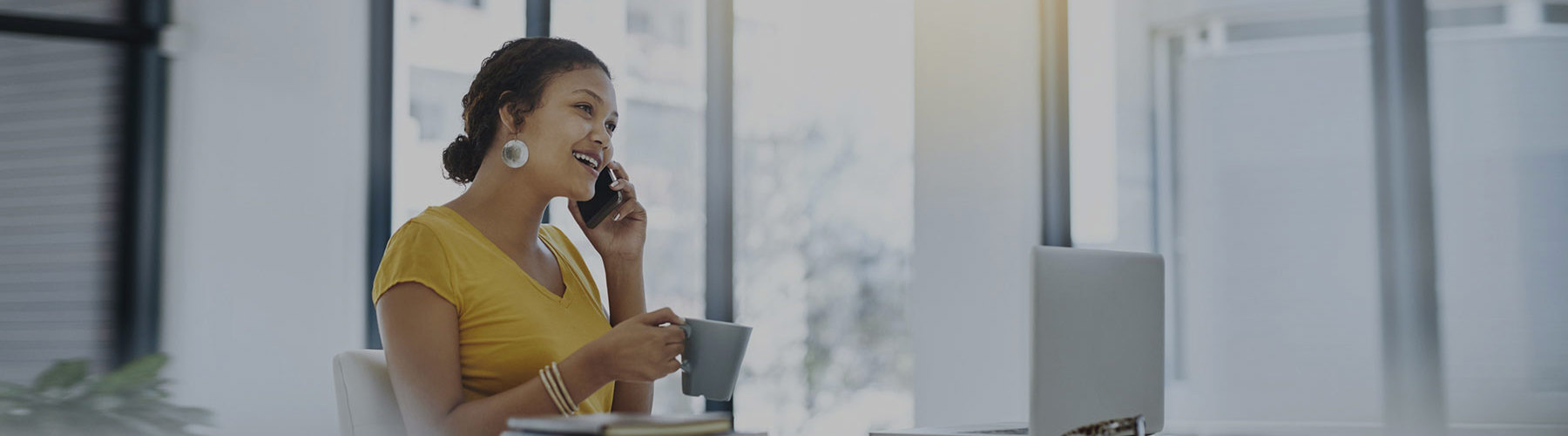Woman on phone sitting at desk with coffee